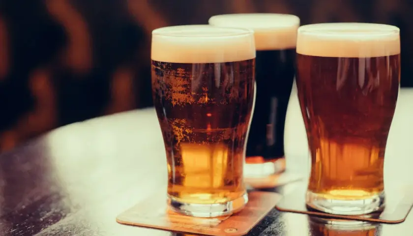 Trois verres de bière irlandaise connue, dont une stout foncée, sur une table.