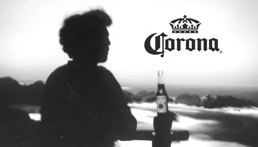 Silhouette d'une personne contemplant la mer, une bouteille de bière Corona à la main. L'image évoque l'origine de la bière Corona.