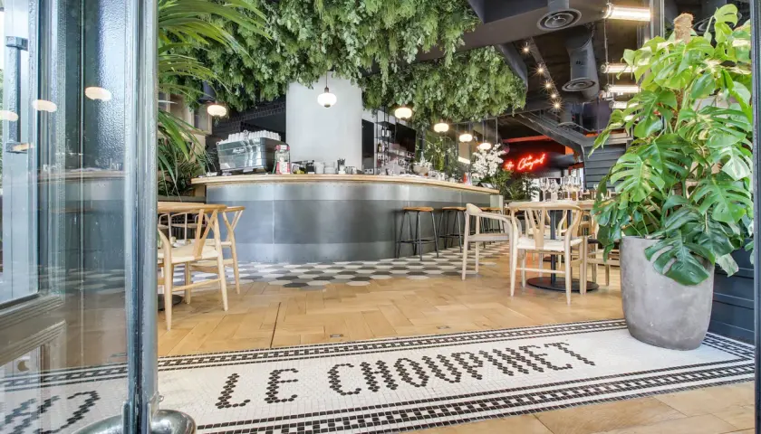 Entrée de la brasserie française "Le Choupinet", décorée de verdure luxuriante et d'un bar moderne.