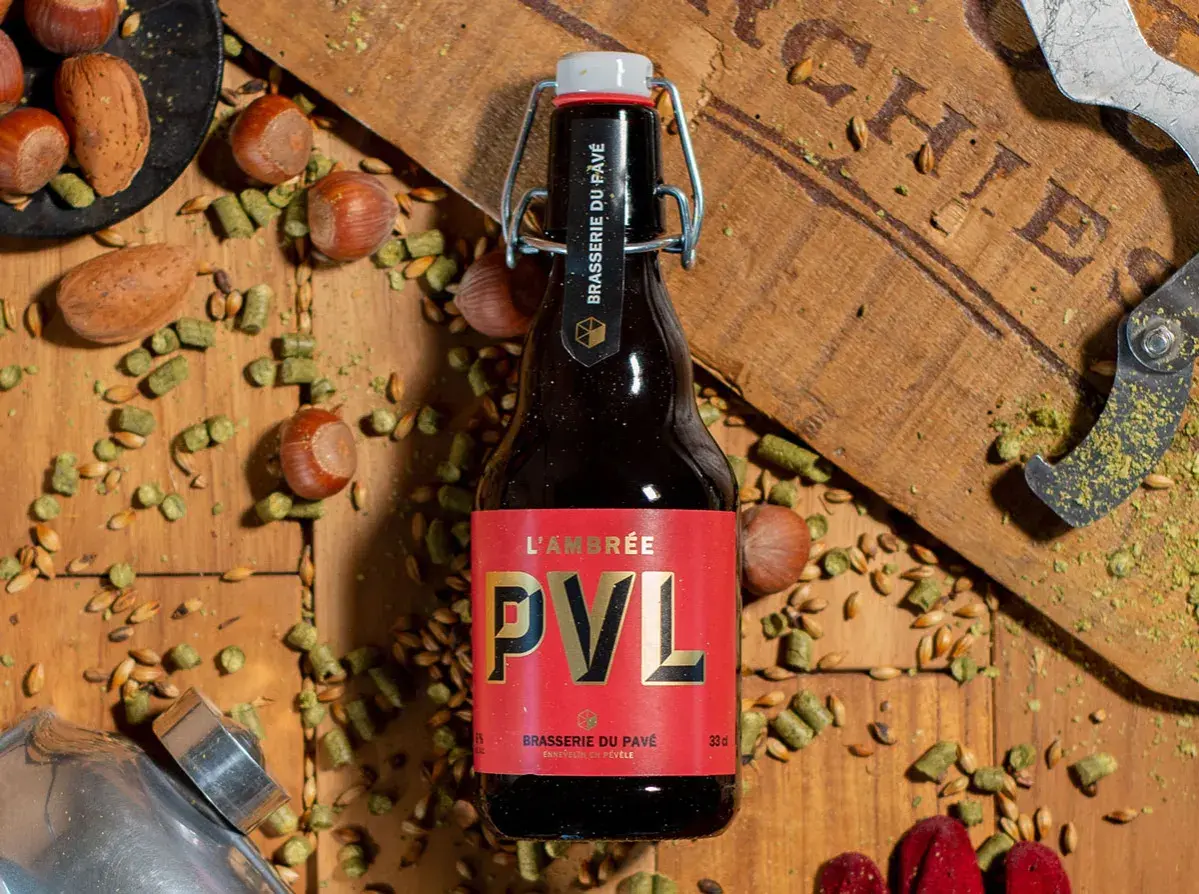 Bouteille de bière brune PVL, entourée de noisettes, de houblon et de grains. Une invitation à découvrir la recette biere brune.