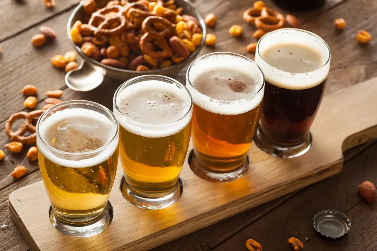Quatre verres de bière, du plus clair au plus foncé, sur un plateau en bois, accompagnés de bretzels et de cacahuètes pour contrebalancer l'amertume.