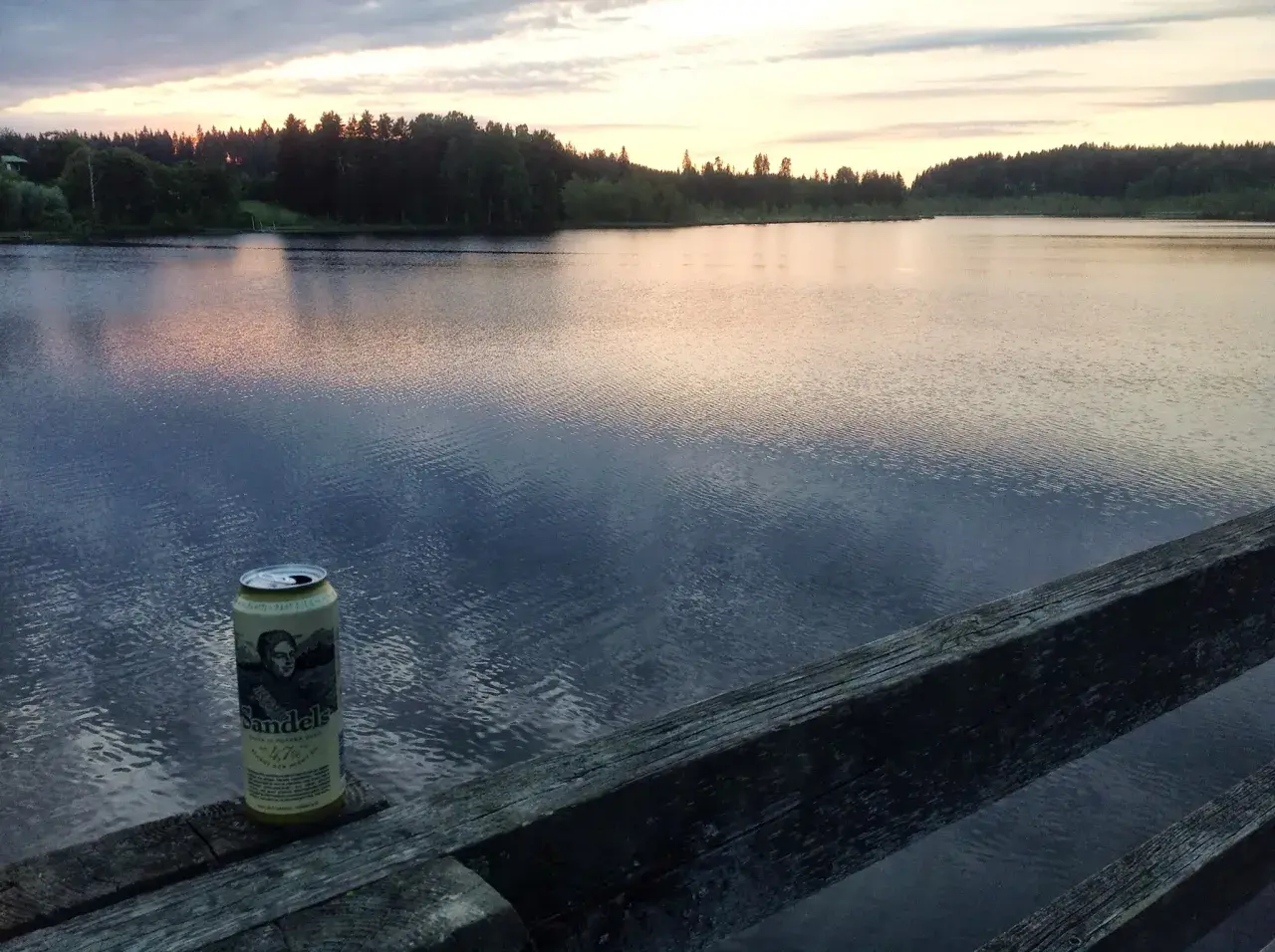 Une canette de bière Sandels, une bière karhu, repose sur un vieux bois au bord d'un lac paisible au coucher du soleil.