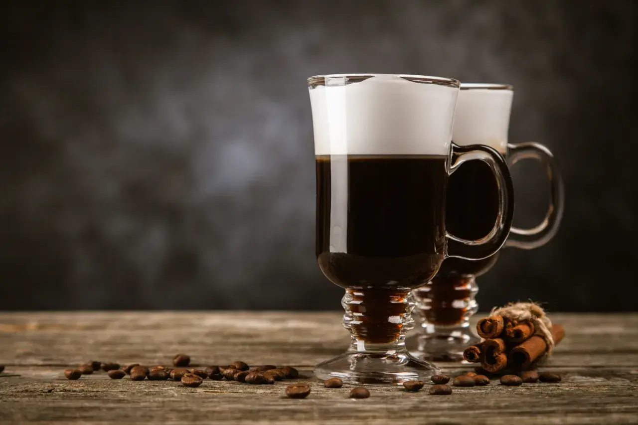 Deux cafés irlandais fumants, parfaits pour une recette irish réconfortante. Grains de café et bâtons de cannelle sur fond sombre.