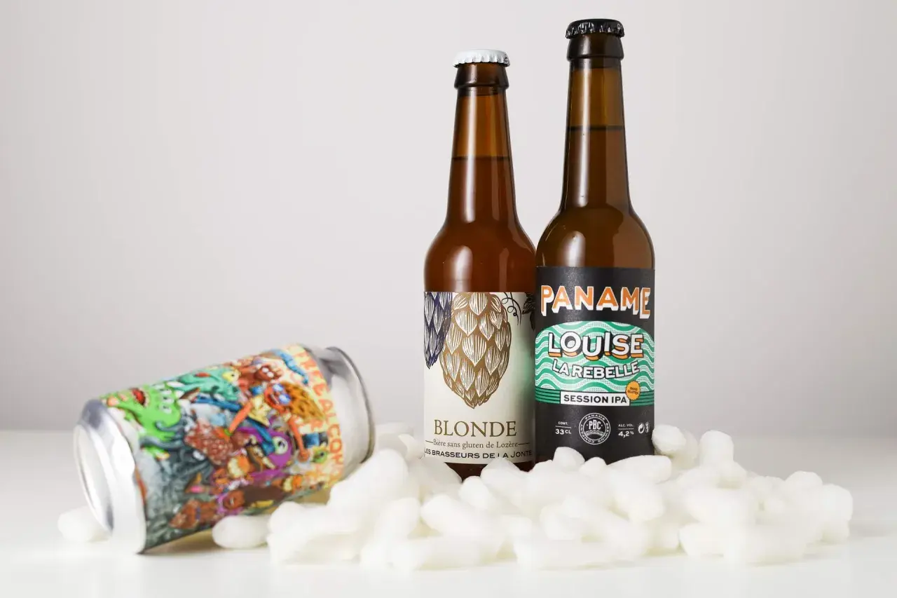 Deux bouteilles de bière et une canette colorée, dont une "Session IPA", reposent sur des flocons blancs.
