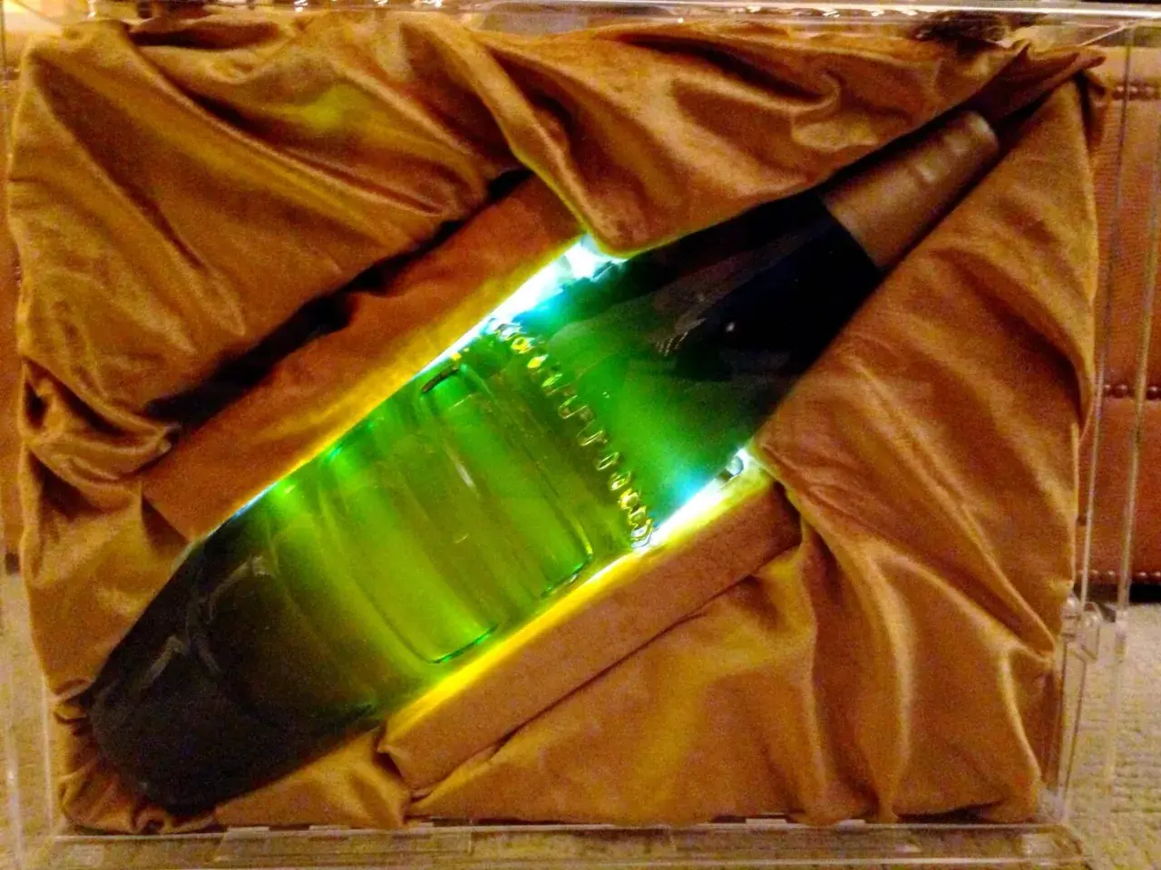 Une bouteille verte lumineuse, peut-être la bière la plus chère du monde, est présentée dans un écrin de tissu doré.