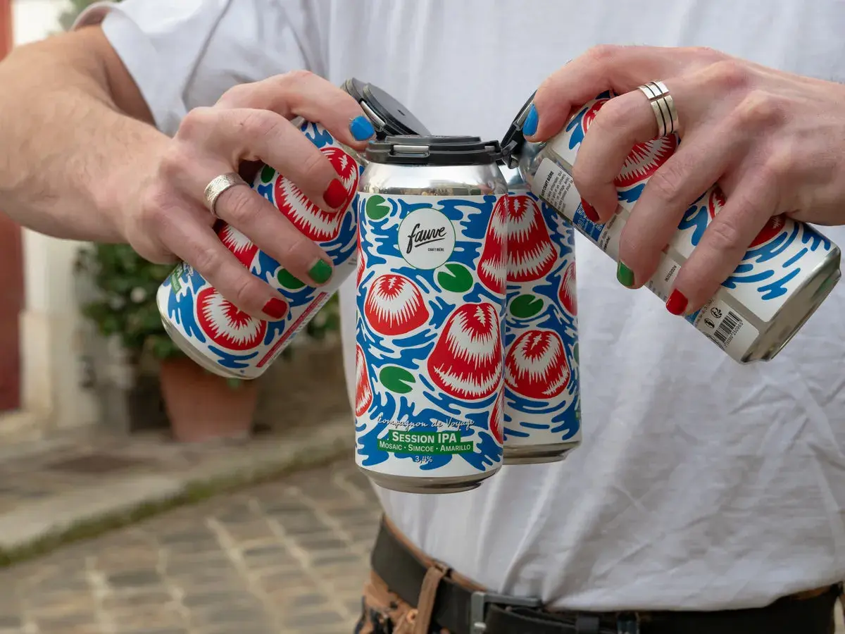 Main d'une personne aux ongles colorés manipulant des canettes de bière Fauve Session IPA.