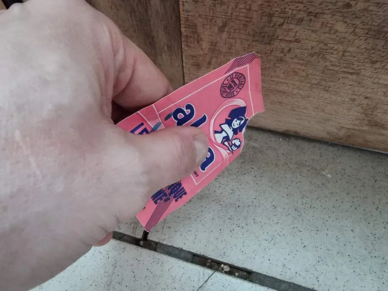Main tenant une étiquette rose, peut-être de levure périmée 1 an, avec une illustration de femme.