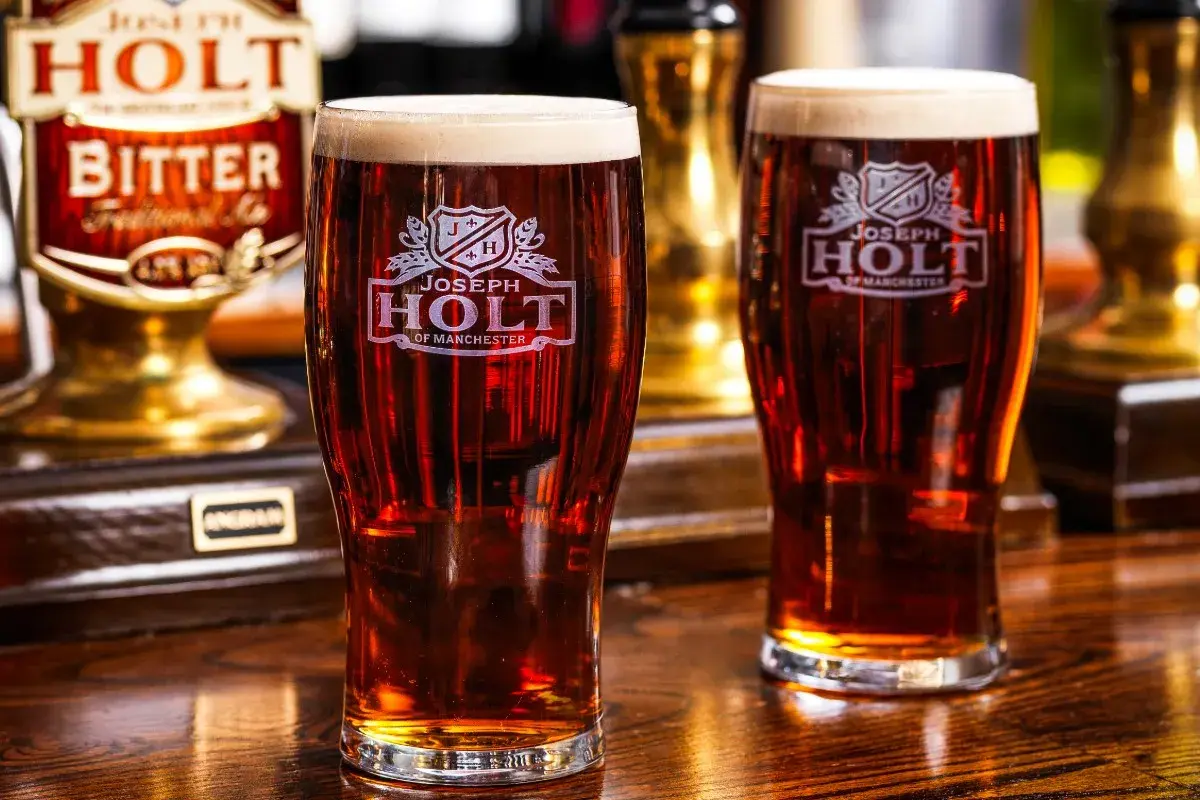 Deux verres de bière ambrée, une cask ale Joseph Holt, sur un comptoir en bois.
