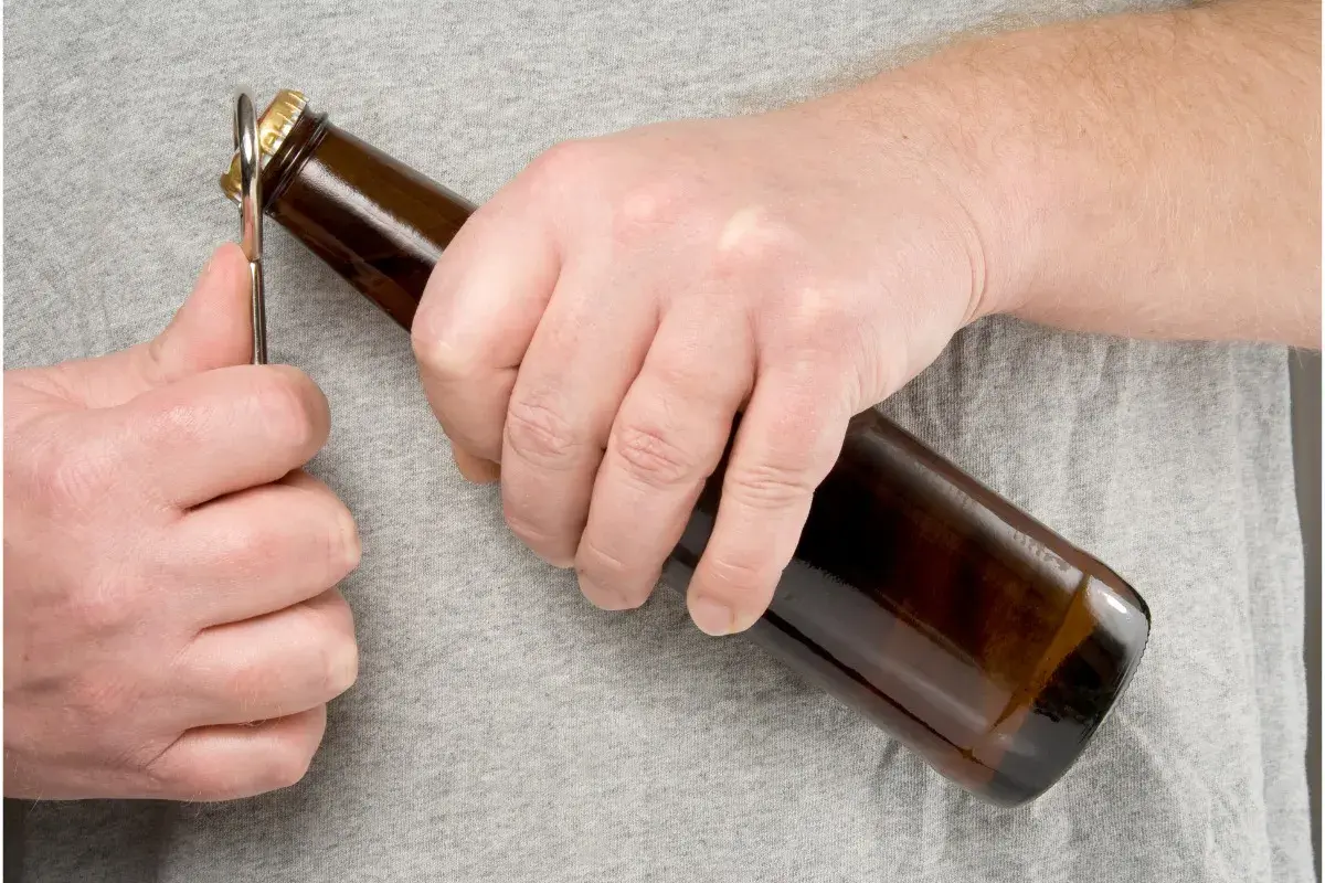 Main gauche ouvrant une bouteille de bière avec un décapsuleur. L'embouteillage bière est imminent.