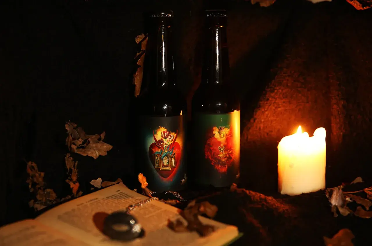 Deux bouteilles de bière la débauche 27 degré, éclairées par une bougie, entourées de feuilles mortes et d'un livre ouvert.