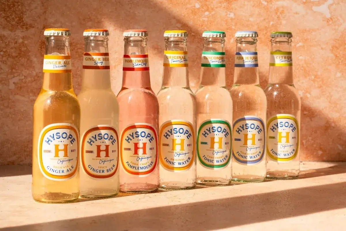 Sept bouteilles de bière et de tonic Hysopé alignées, avec des saveurs comme le gingembre et le pamplemousse, évoquant un apéritif en Italie.