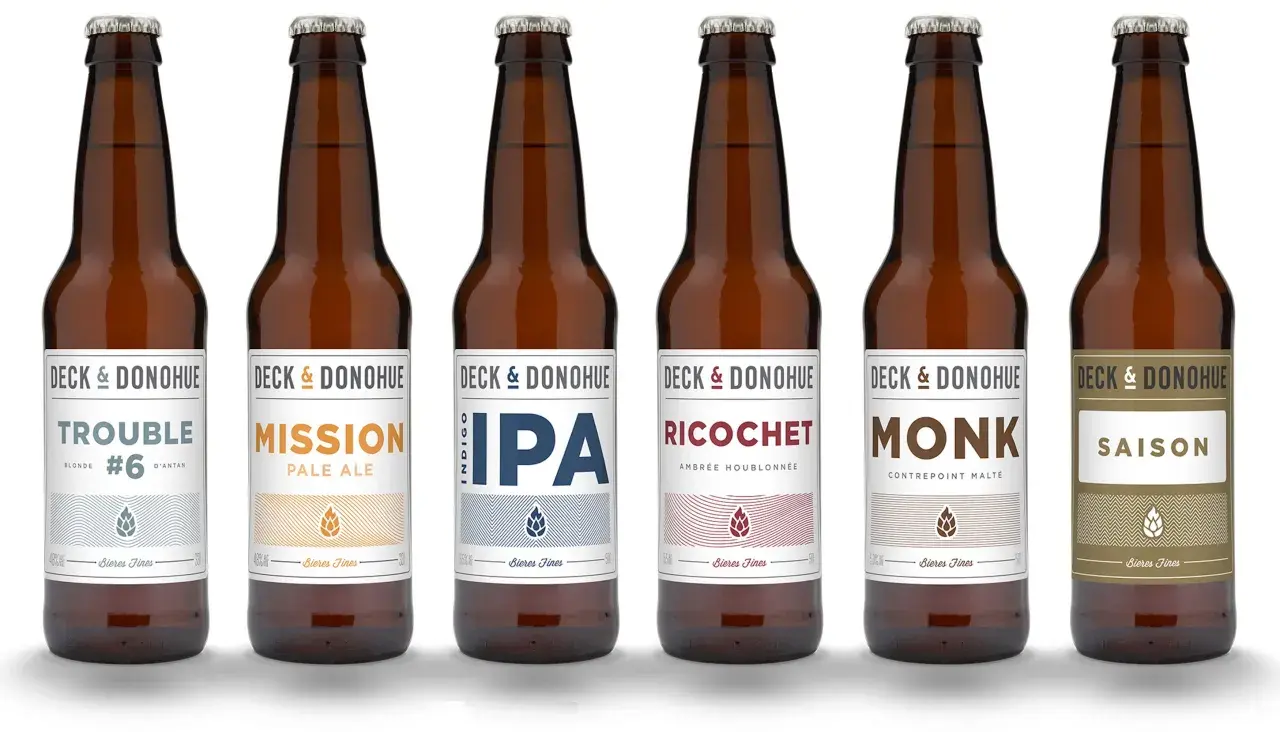Six bouteilles de bière de la marque Deck & Donohue, proposant différents types de bière : Trouble, Mission, IPA, Ricochet, Monk et Saison.