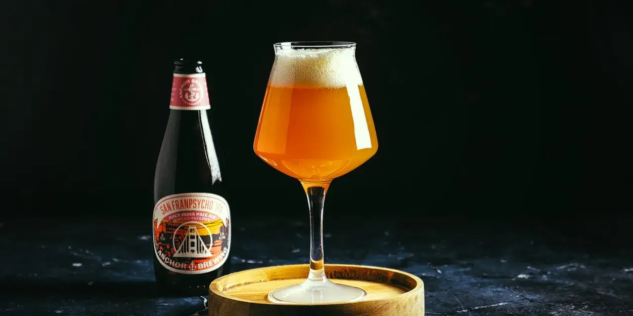 Une bouteille et un verre de bière ambrée Anchor, avec une mousse généreuse. L'étiquette de la bière mentionne "Anchor Brewing".