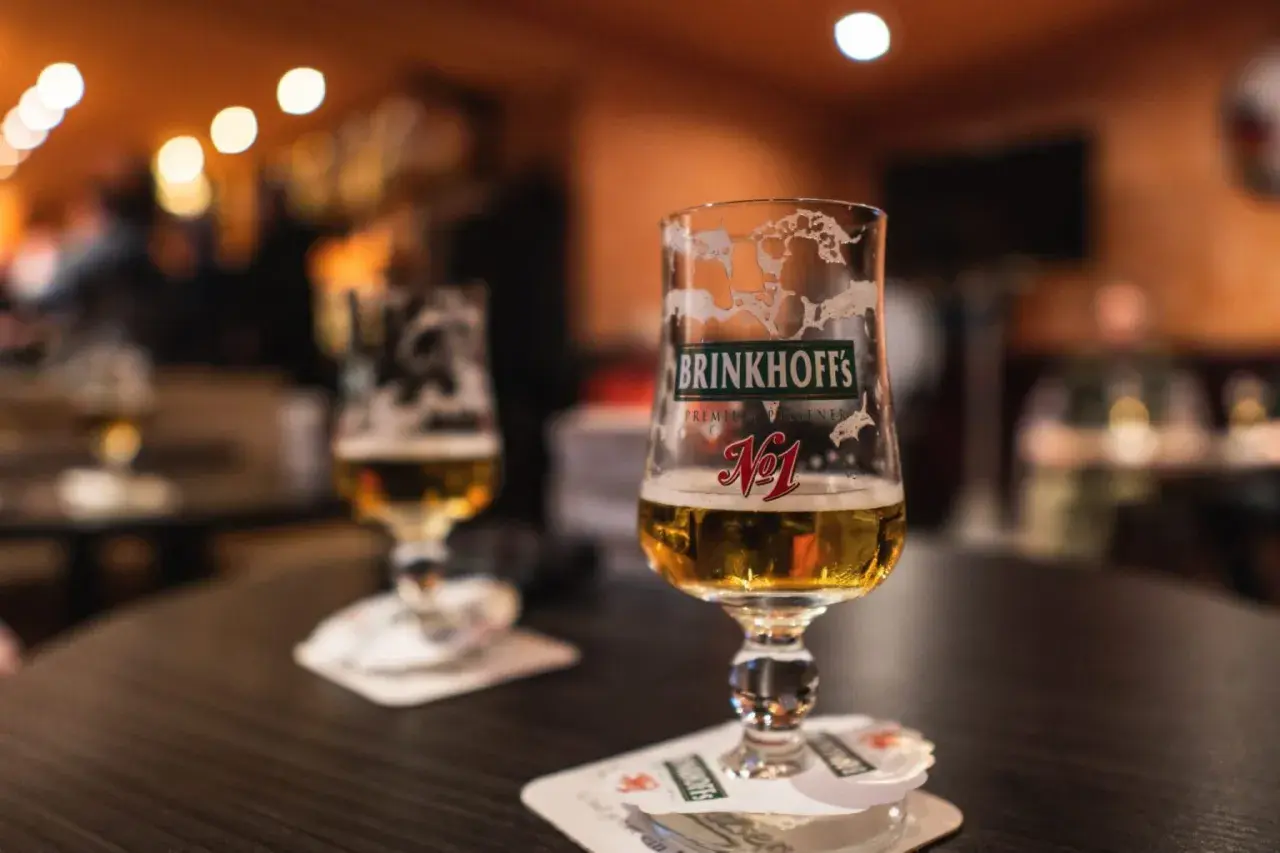 Deux verres de bières allemandes Brinkhoff's, l'un à moitié plein, sur une table sombre.