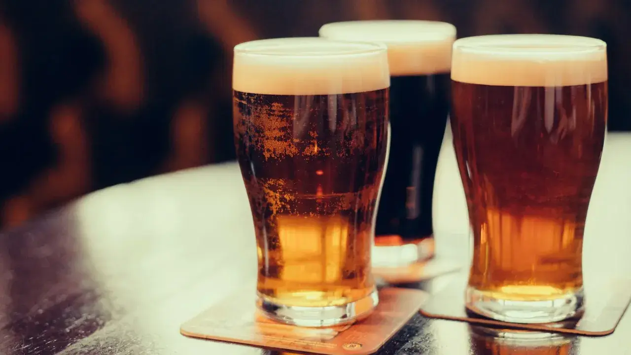 Trois verres de bière irlandaise connue, dont une stout foncée, sur une table.