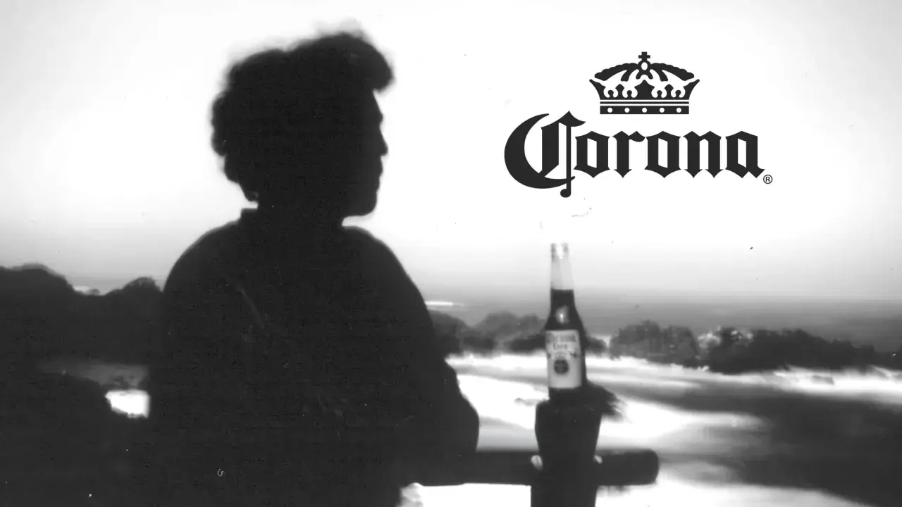 Silhouette d'une personne contemplant la mer, une bouteille de bière Corona à la main. L'image évoque l'origine de la bière Corona.