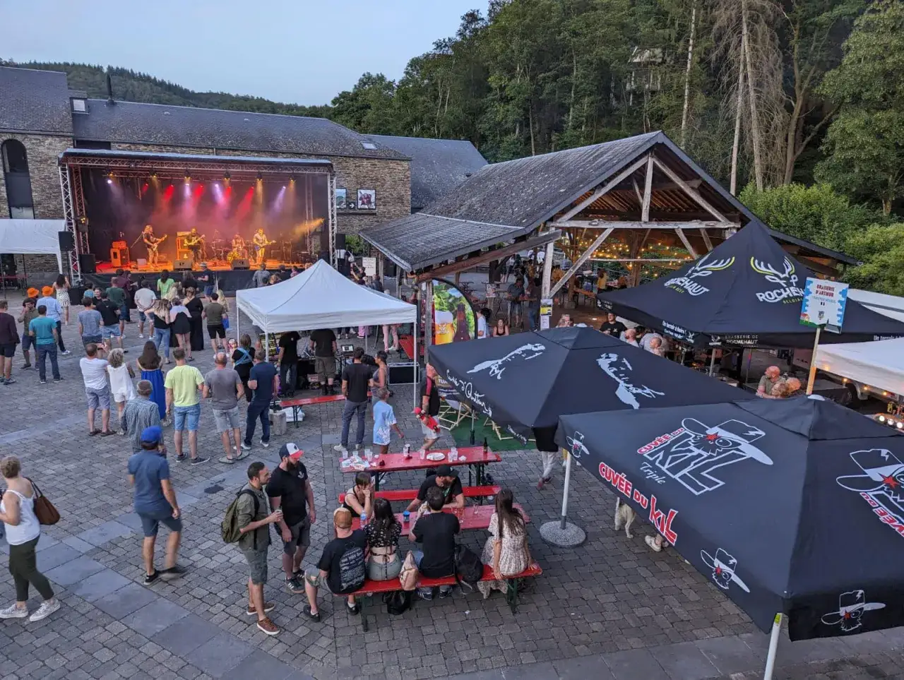 Ambiance de fête de la bière avec concert en plein air, tentes et foule joyeuse profitant de la soirée.