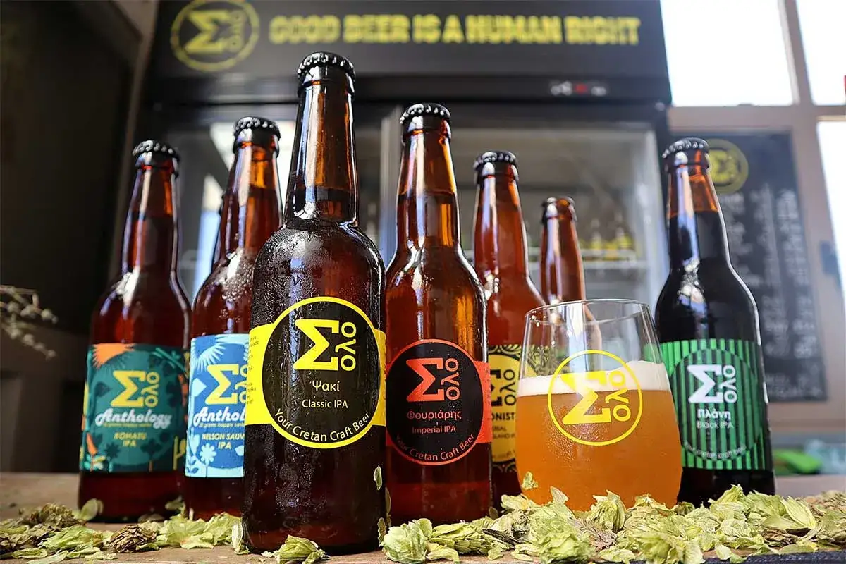 Une sélection de bières artisanales crétoises, dont une IPA classique et une IPA impériale, présentées avec un verre de bière et du houblon.