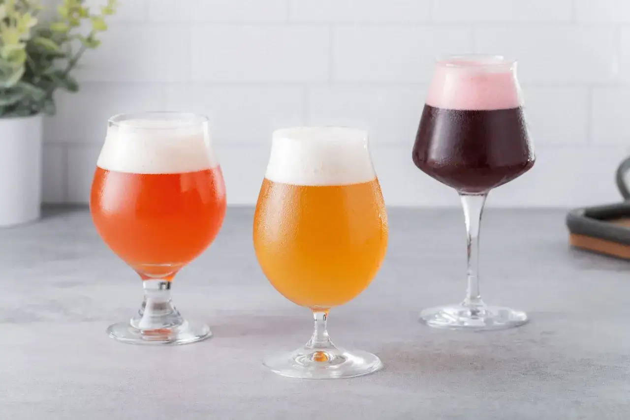 Trois verres de bière acide aux couleurs vives : rouge orangé, jaune doré et pourpre avec une mousse rose.