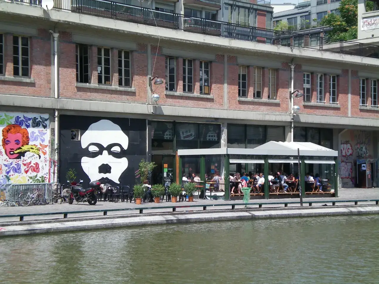 Terrasse anim&eacute;e devant la Paname Brewing Company, avec une grande fresque murale et un canal.