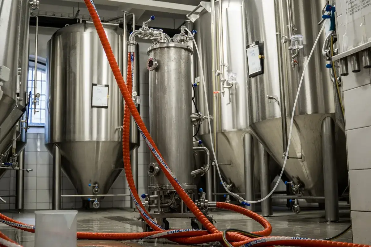 Cuve en acier inoxydable dans une brasserie, avec des tuyaux rouges qui semblent hop creep.