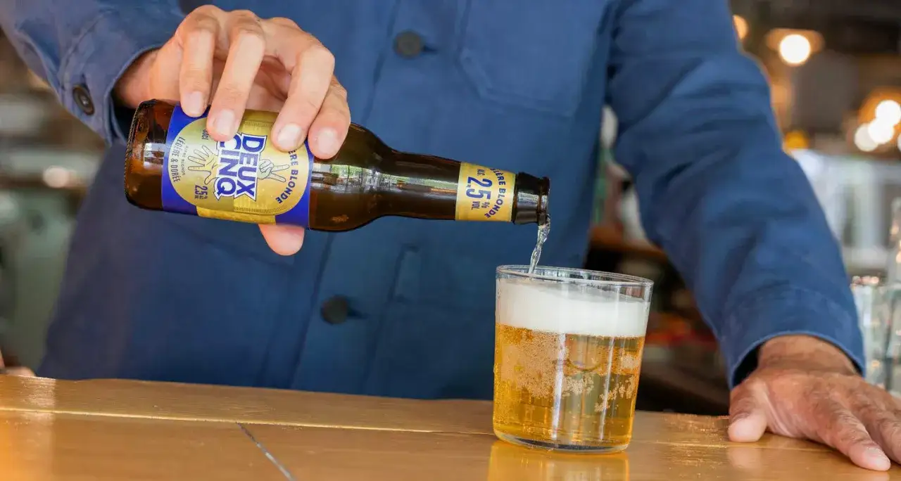 Une main verse une bière blonde légère et dorée, une bière pas forte à 2.5% vol, dans un verre.