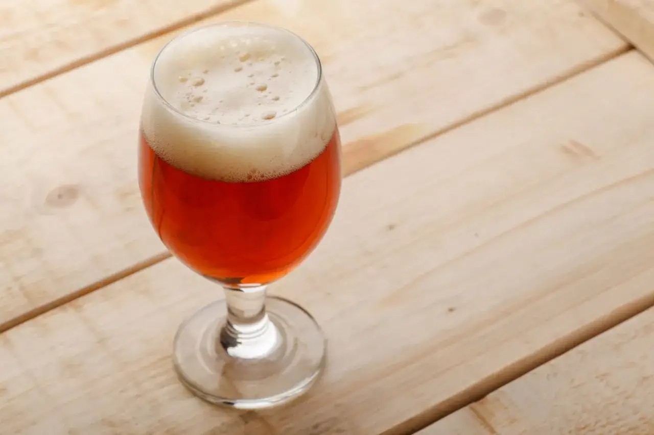Verre de Belgian Pale Ale ambrée, sur fond de planches de bois claires.