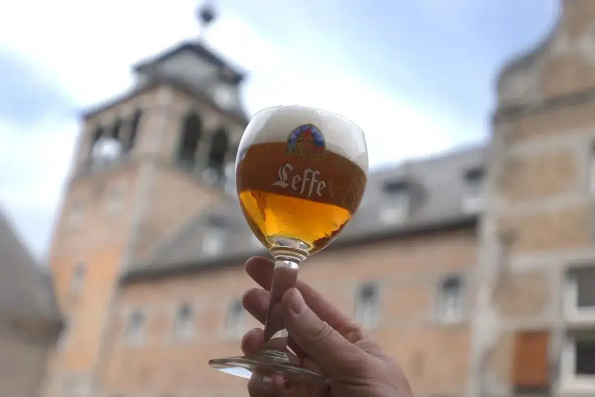 Verre de bière Leffe, avec le logo bien visible, devant un bâtiment historique.