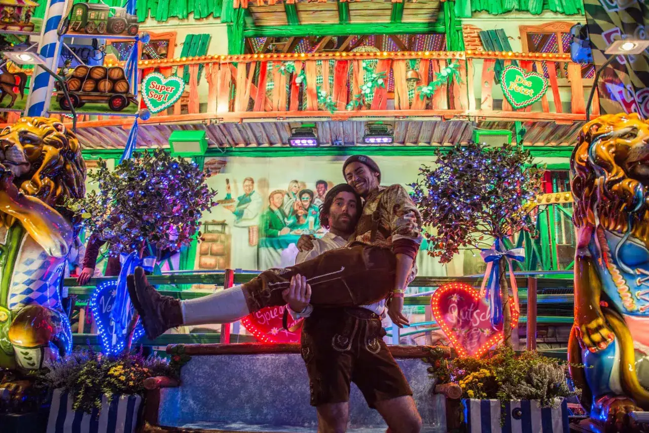 Un couple en tenue bavaroise s'amuse, peut-&ecirc;tre lors d'une date fete de la biere allemagne. Lumi&egrave;res vives, d&eacute;corations festives et lions dor&eacute;s cr&eacute;ent une ambiance joyeuse.