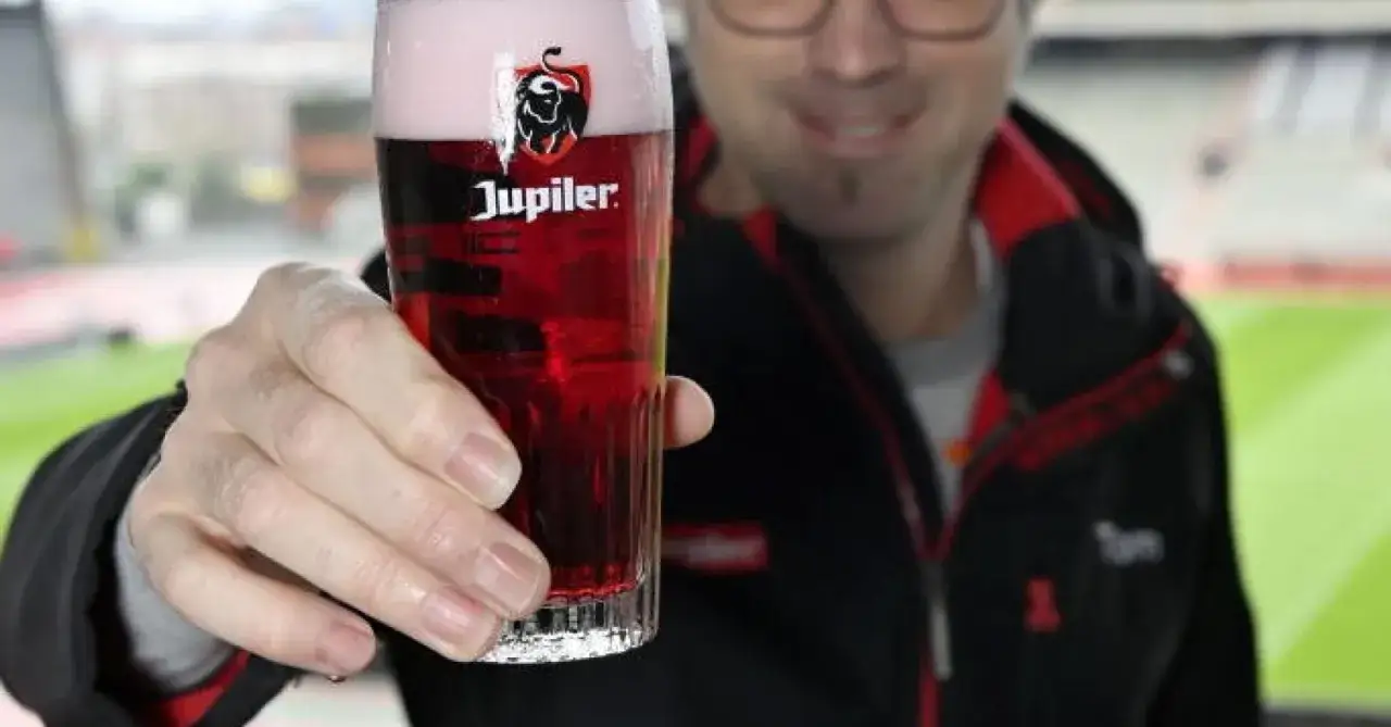 Un homme tient un verre de bière Jupiler rouge, parfait pour apprécier son degré alcool.