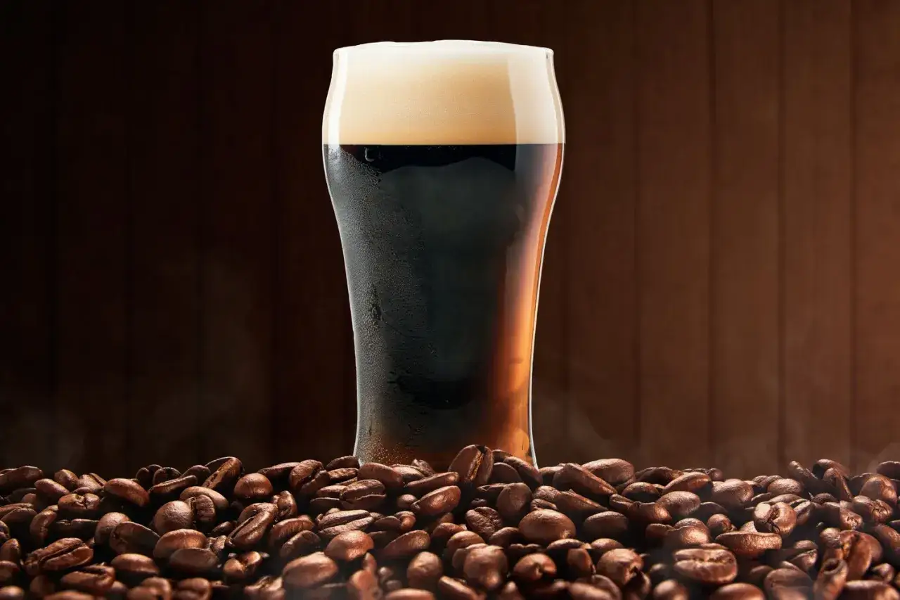 Verre de bi&egrave;re brune mousseuse sur fond de grains de caf&eacute; torr&eacute;fi&eacute;s. Une invitation &agrave; d&eacute;couvrir la recette biere brune.
