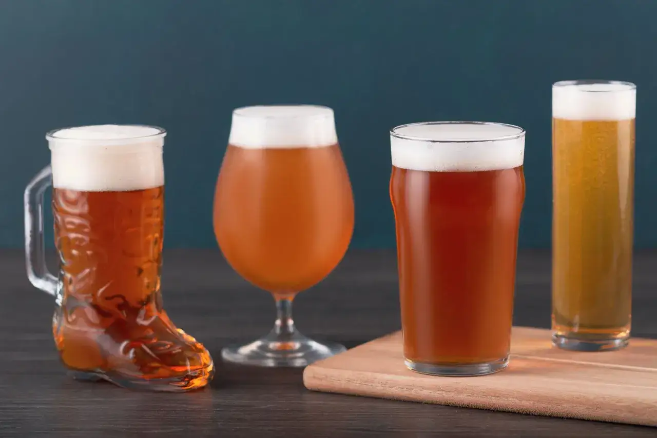 Quatre verres de bi&egrave;re ambr&eacute;e anglaise, dont un en forme de botte, sur une table en bois sombre.