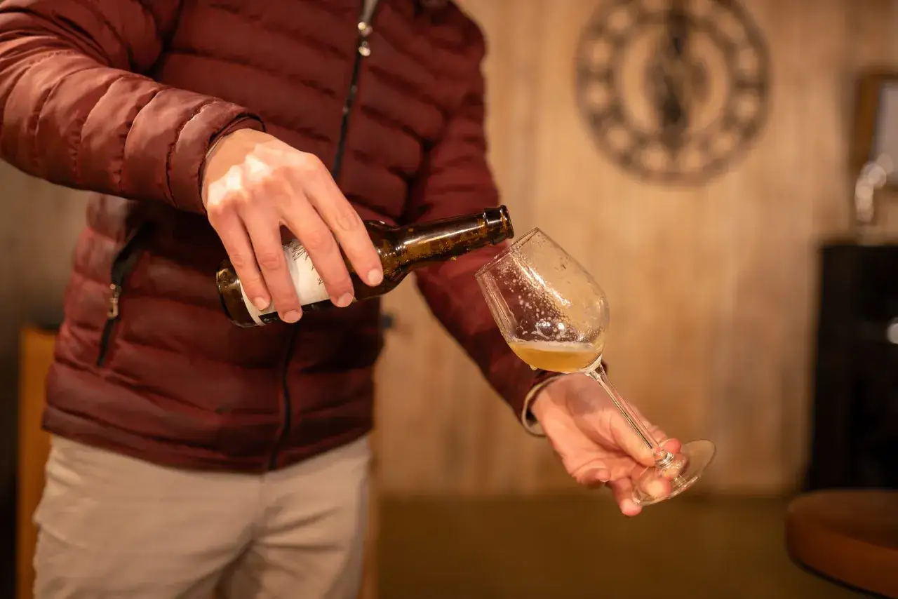 Un homme verse une bière blonde dans un verre. La mousse déborde légèrement, rappelant la douceur d'une journée d'été.