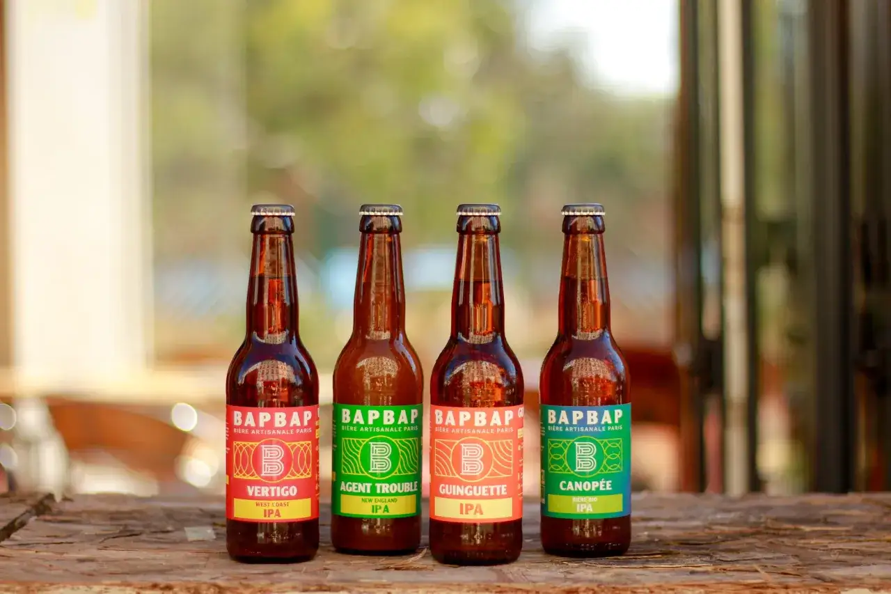 Quatre bouteilles de bière artisanale BAPBAP, dont une NEIPA, sur une table en bois.