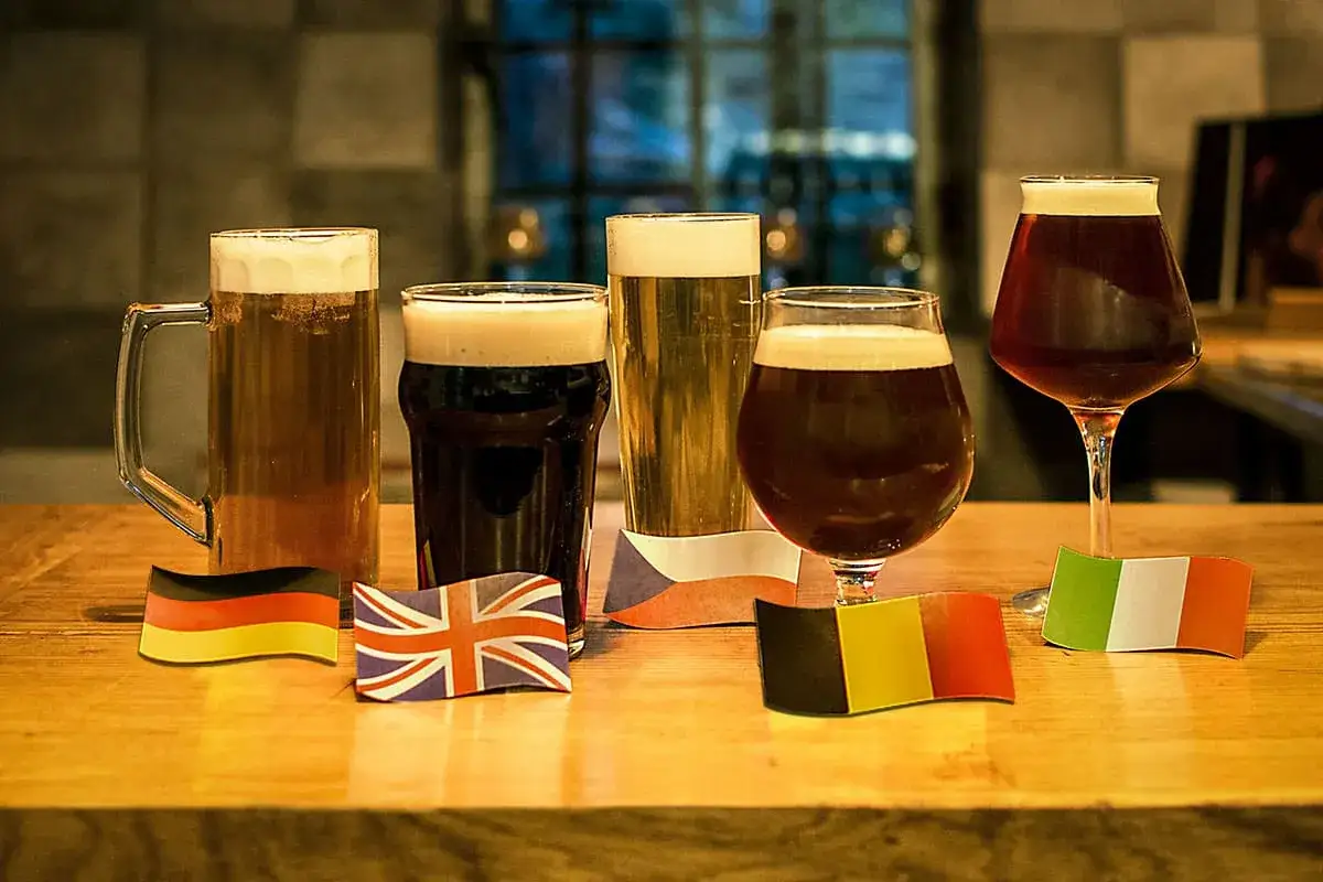 Cinq bières aux couleurs variées, de la blonde à la brune, alignées avec des drapeaux européens.