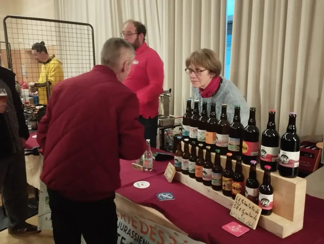 Des bouteilles de bière sont présentées lors d'une fête de la bière. Un homme discute avec une vendeuse.