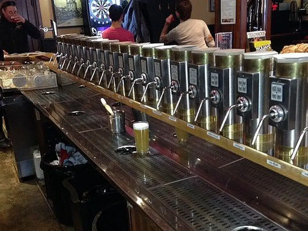 Une rangée impressionnante de tireuses à bière, prêtes à servir une délicieuse cask ale. Un barman boit une bière, un verre de bière est posé sur le comptoir.
