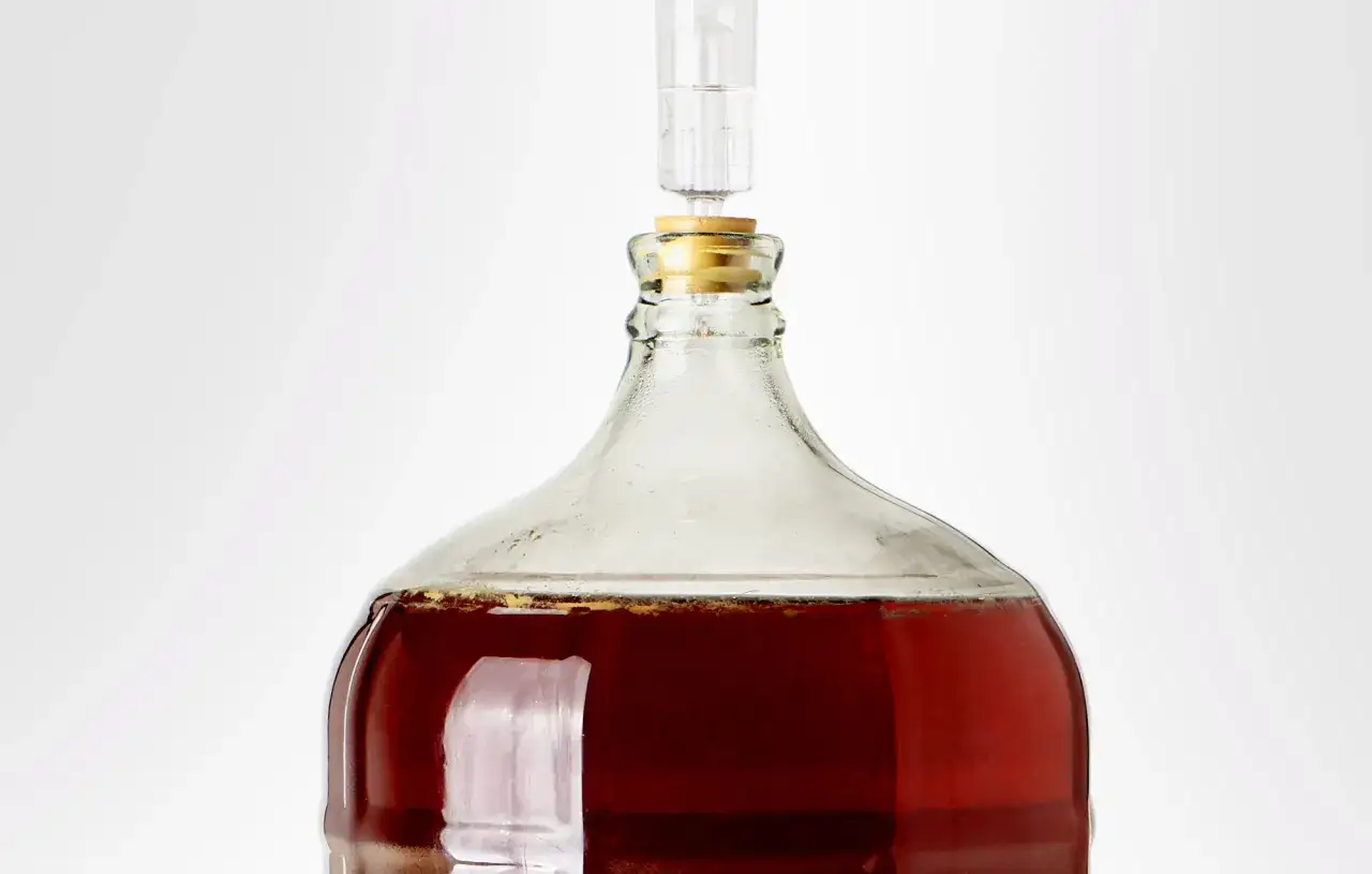 Bouteille en verre remplie de liquide ambré, prête pour la fermentation secondaire de bière. Un barboteur est inséré dans le bouchon.