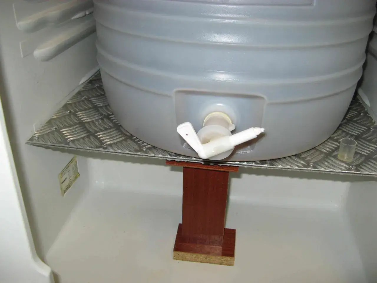 Un grand r&eacute;cipient de bi&egrave;re en cours de cold crash dans un r&eacute;frig&eacute;rateur, sur une &eacute;tag&egrave;re en m&eacute;tal.