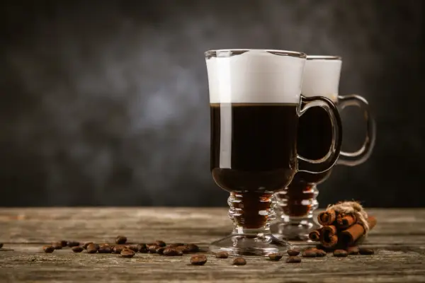 Deux cafés irlandais fumants, parfaits pour une recette irish réconfortante. Grains de café et bâtons de cannelle sur fond sombre.