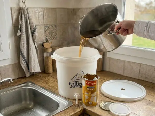 Préparation d'une bière de saison : on verse le moût d'une marmite dans un fermenteur. Une boîte de Pilsner est à côté.