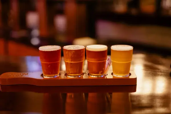 Quatre verres de bière, de différentes couleurs, sur un plateau en bois. Une dégustation de bière, pas de bière chaude ici !